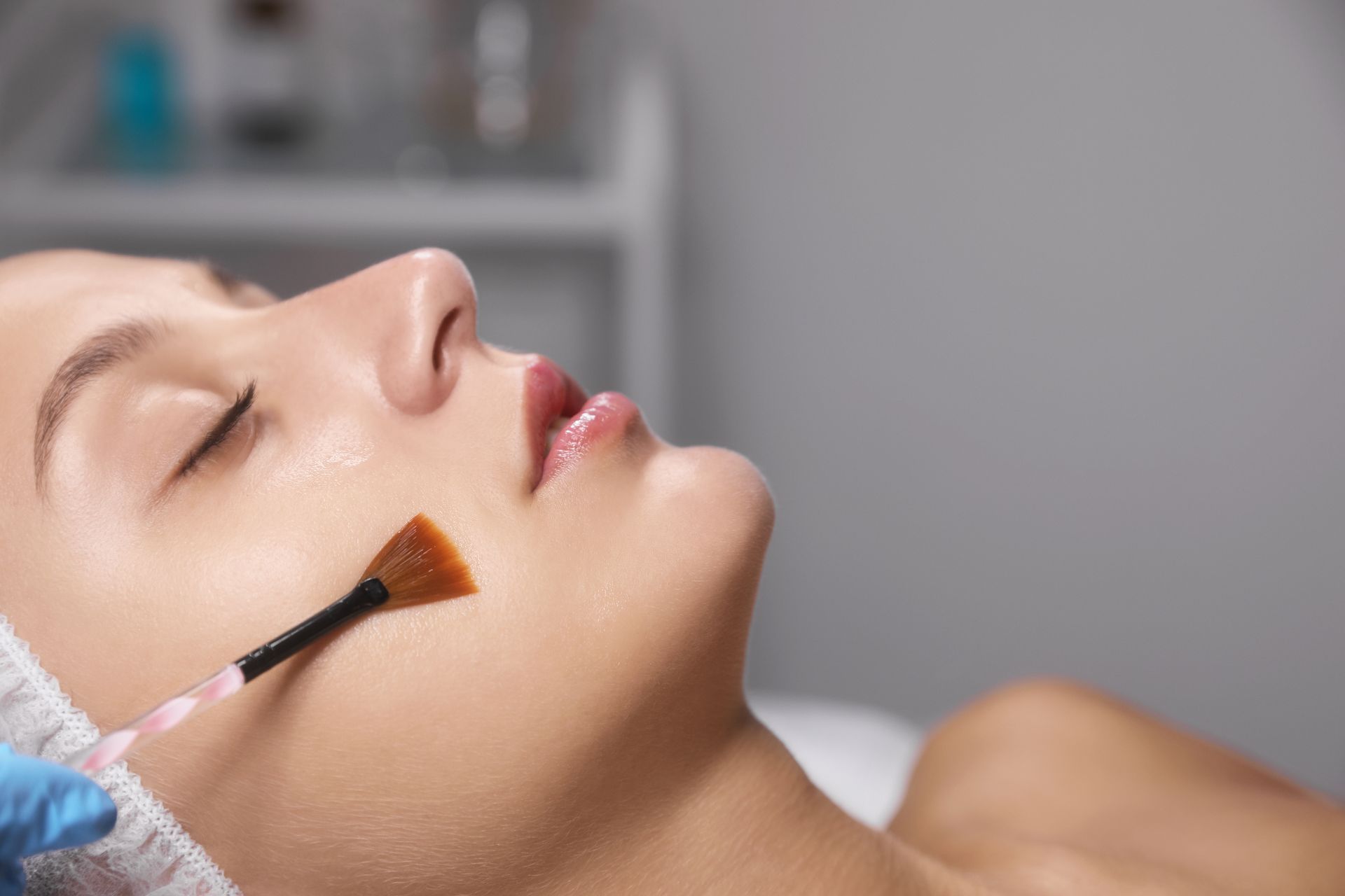 A woman is getting a facial treatment with a brush on her face.
