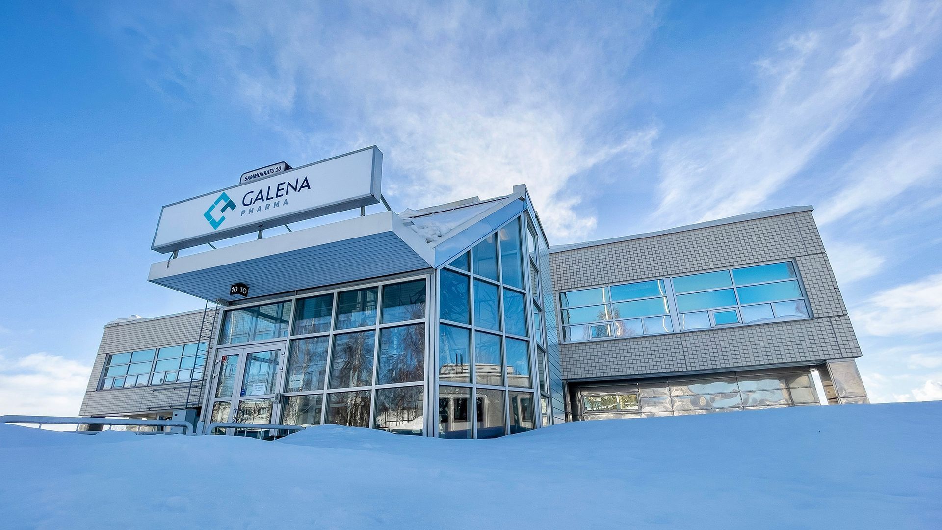 Modern building with glass facade, snowy setting, and blue sky. The sign reads, 