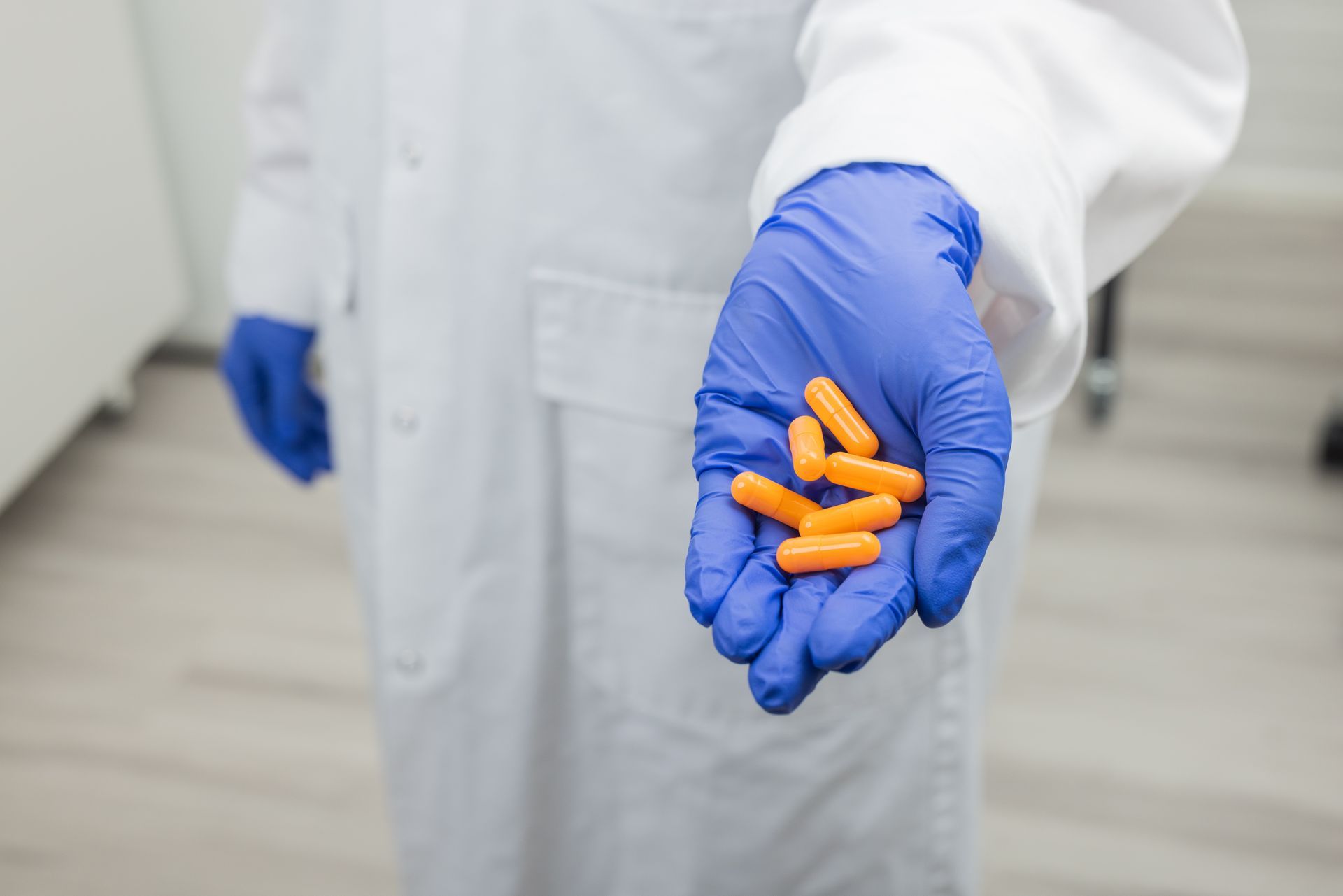 Person in lab coat and blue gloves holding orange capsules.