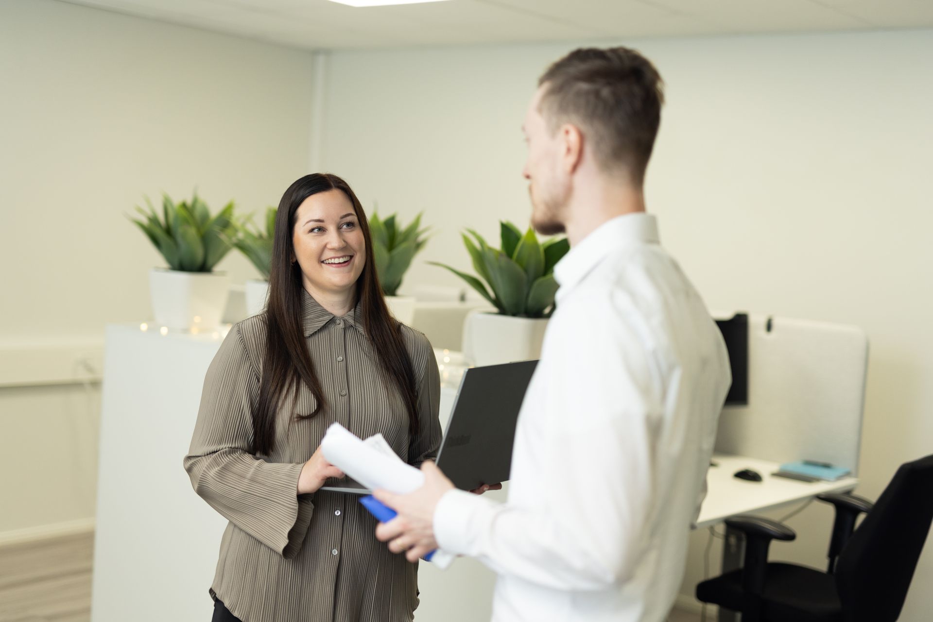 Woman in brown shirt smiles at man holding papers in a bright office.