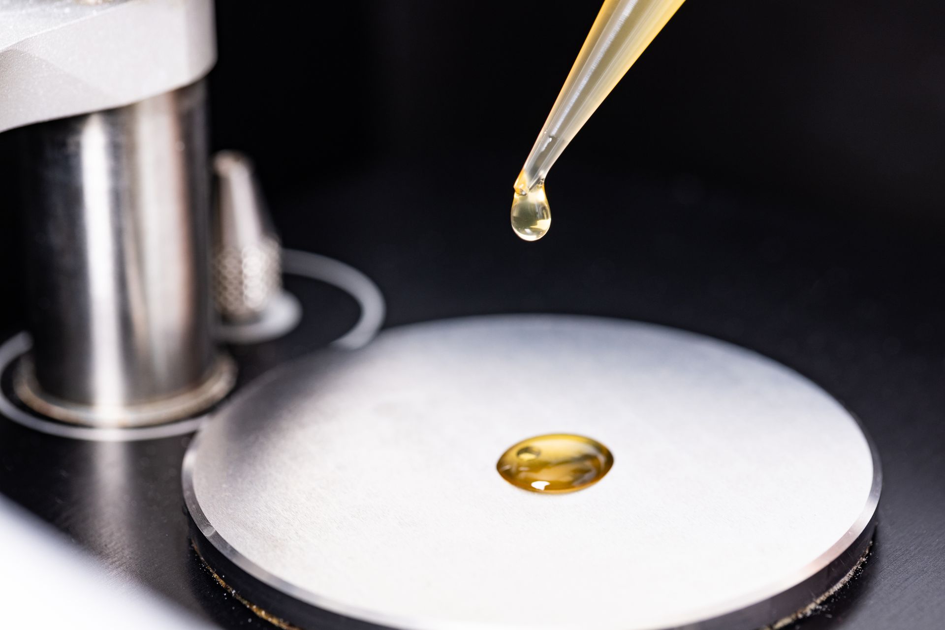 Dropper dispensing yellow liquid onto a silver metal surface.