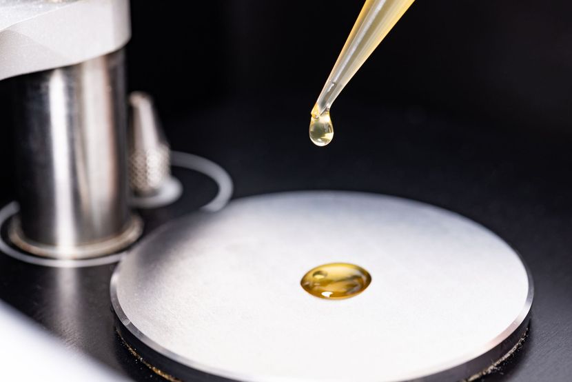 Droplet of yellow liquid falling from a pipette onto a metal surface, close-up view.