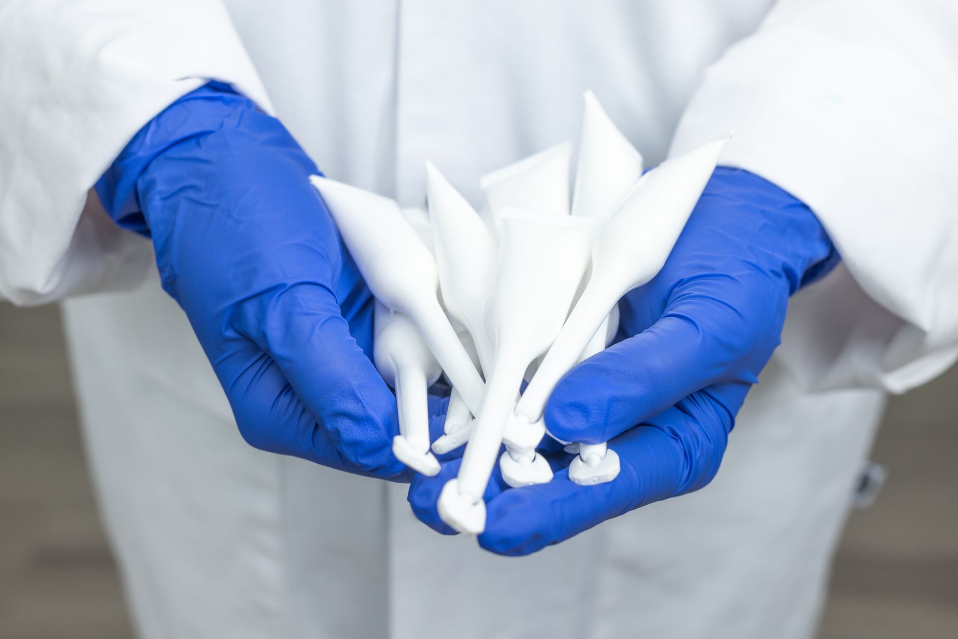 Person in blue gloves and lab coat holding several white, cone-shaped objects.