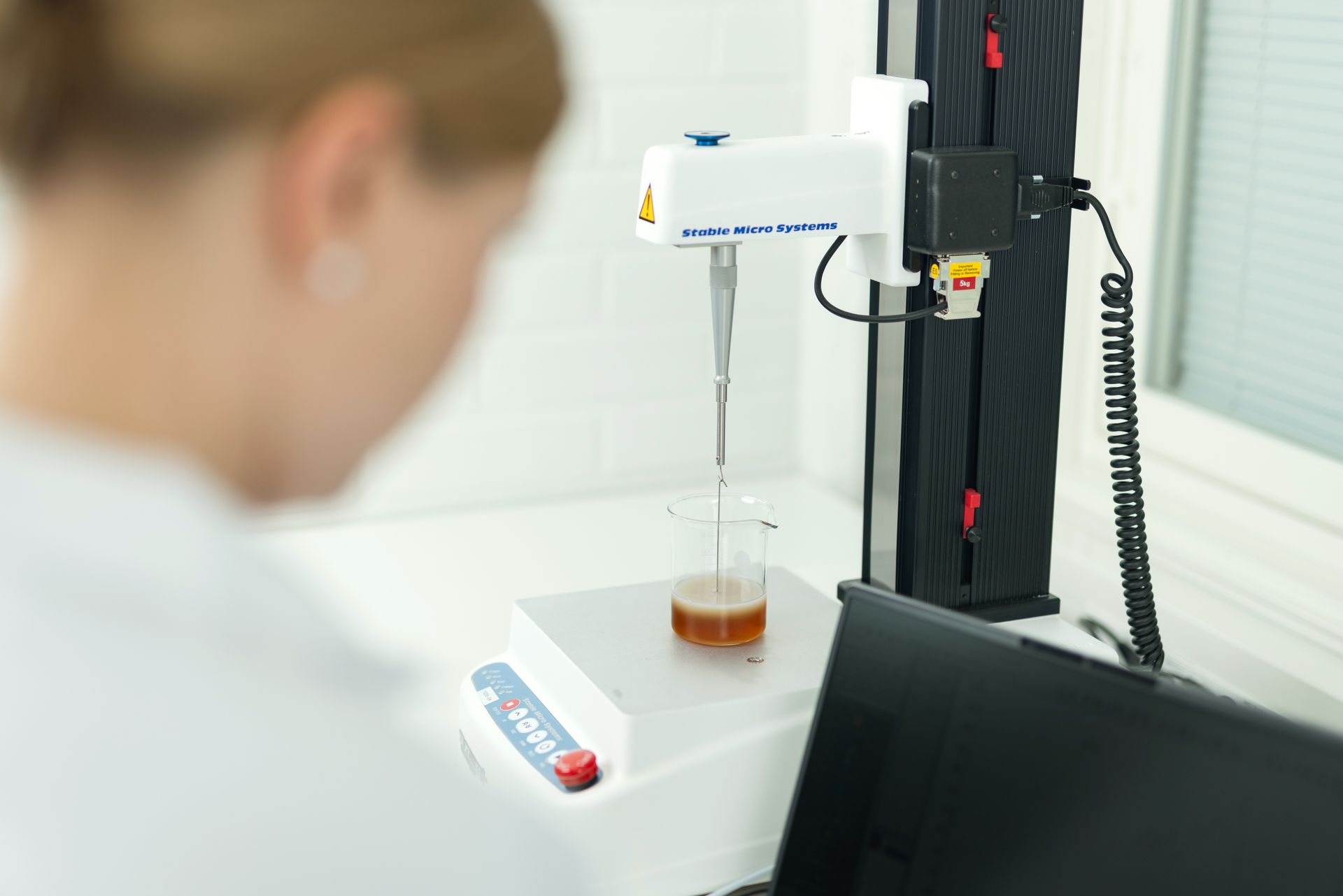 Scientist using automated lab equipment to measure a brown liquid in a beaker.