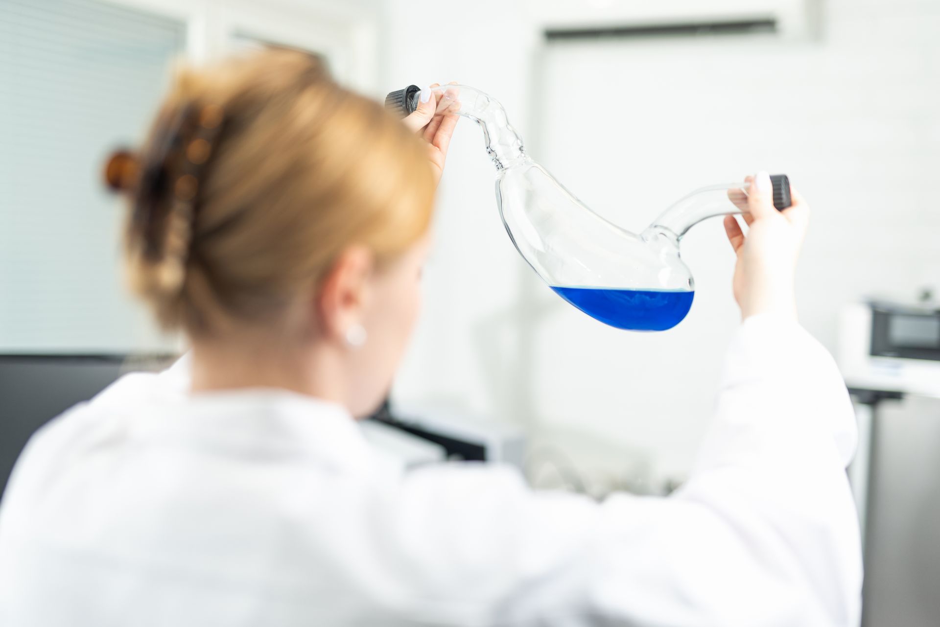 Scientist in a lab coat holding a flask of blue liquid, inspecting it.