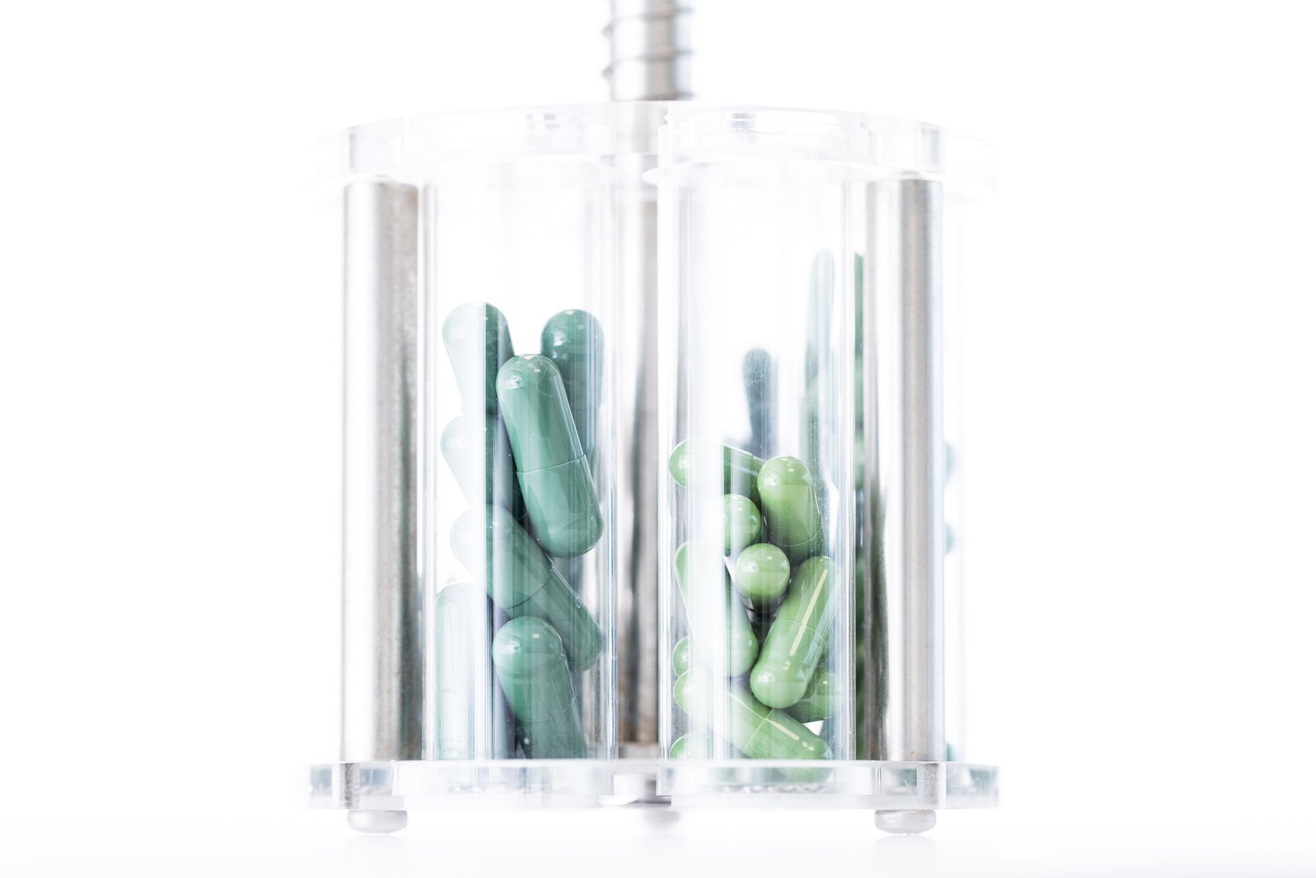 Two clear tubes holding green capsules in a pill dispenser.