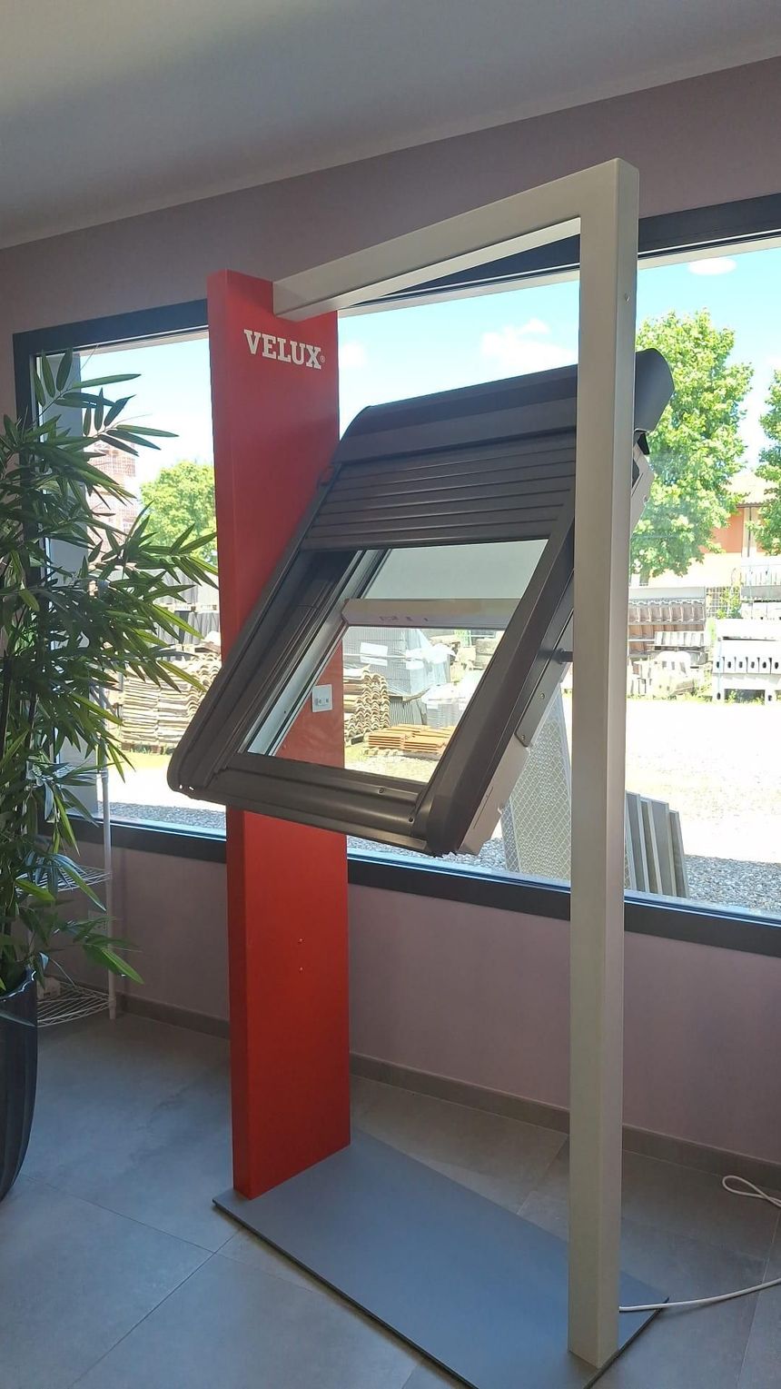 Chiosco espositivo esterno con schermo touchscreen inclinato e pannello verticale rosso, posizionato accanto a una parete vetrata.