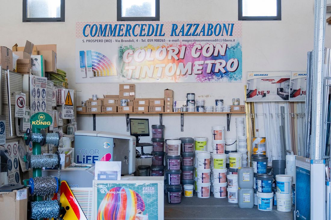 Espositore di un negozio di vernici con prodotti per la miscelazione dei colori, barattoli di vernice e insegne in italiano sopra gli scaffali.