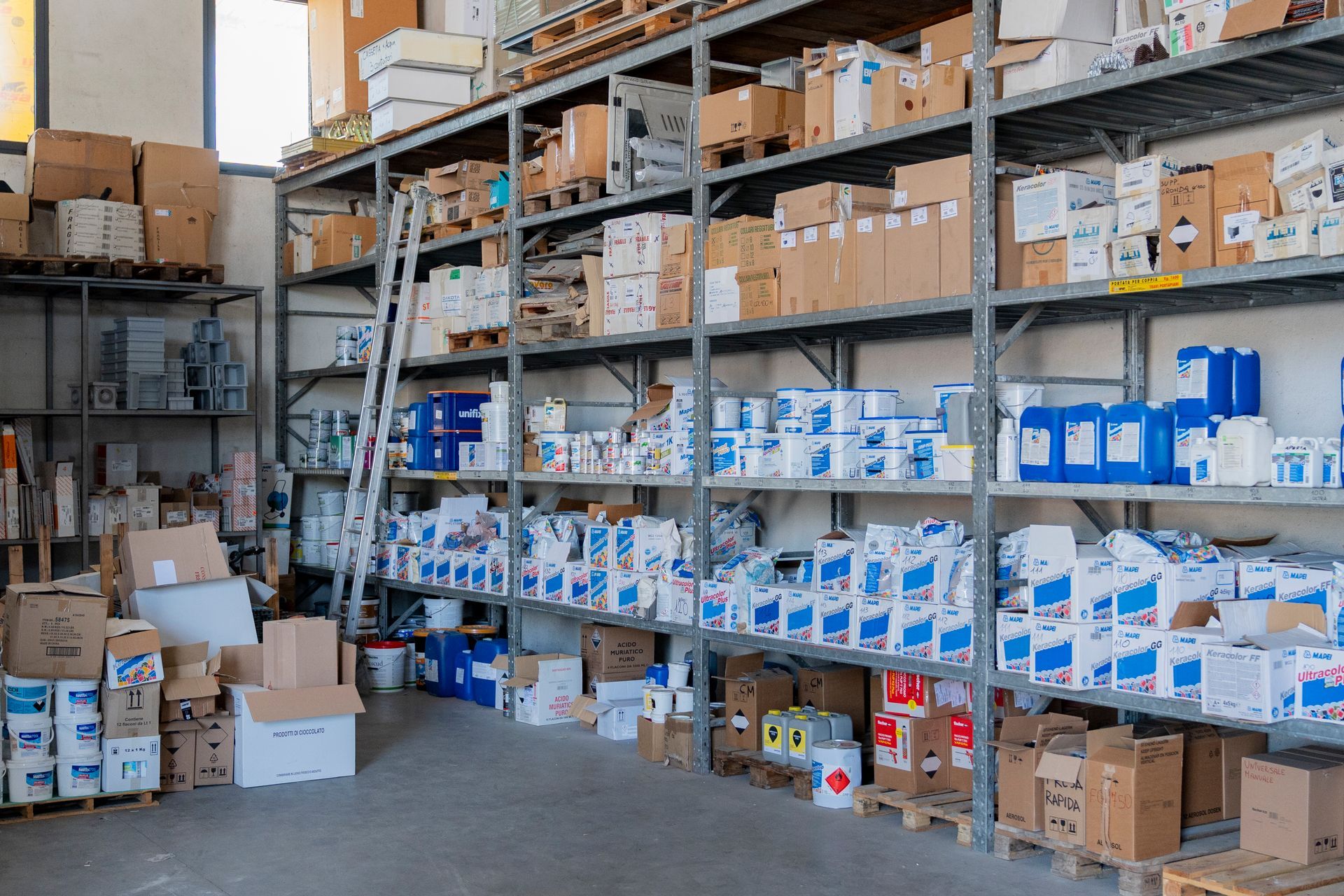 Corridoio del magazzino con scaffali metallici pieni di scatole di cartone e materiali di inventario blu e bianchi.