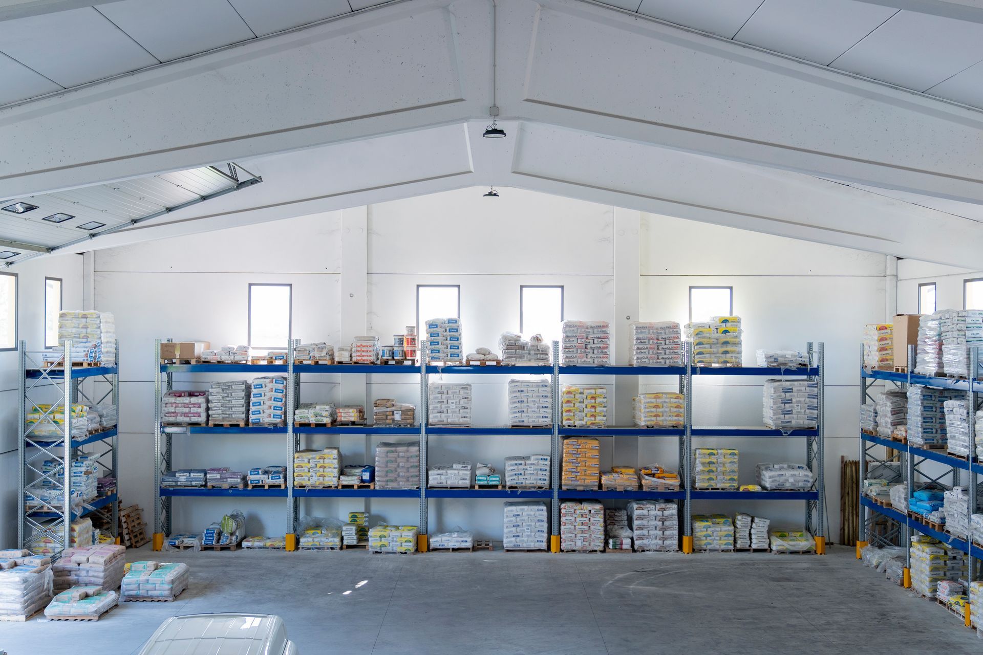 Ampio interno di magazzino con scaffali pieni di scatole e materiali etichettati sotto un alto soffitto bianco.