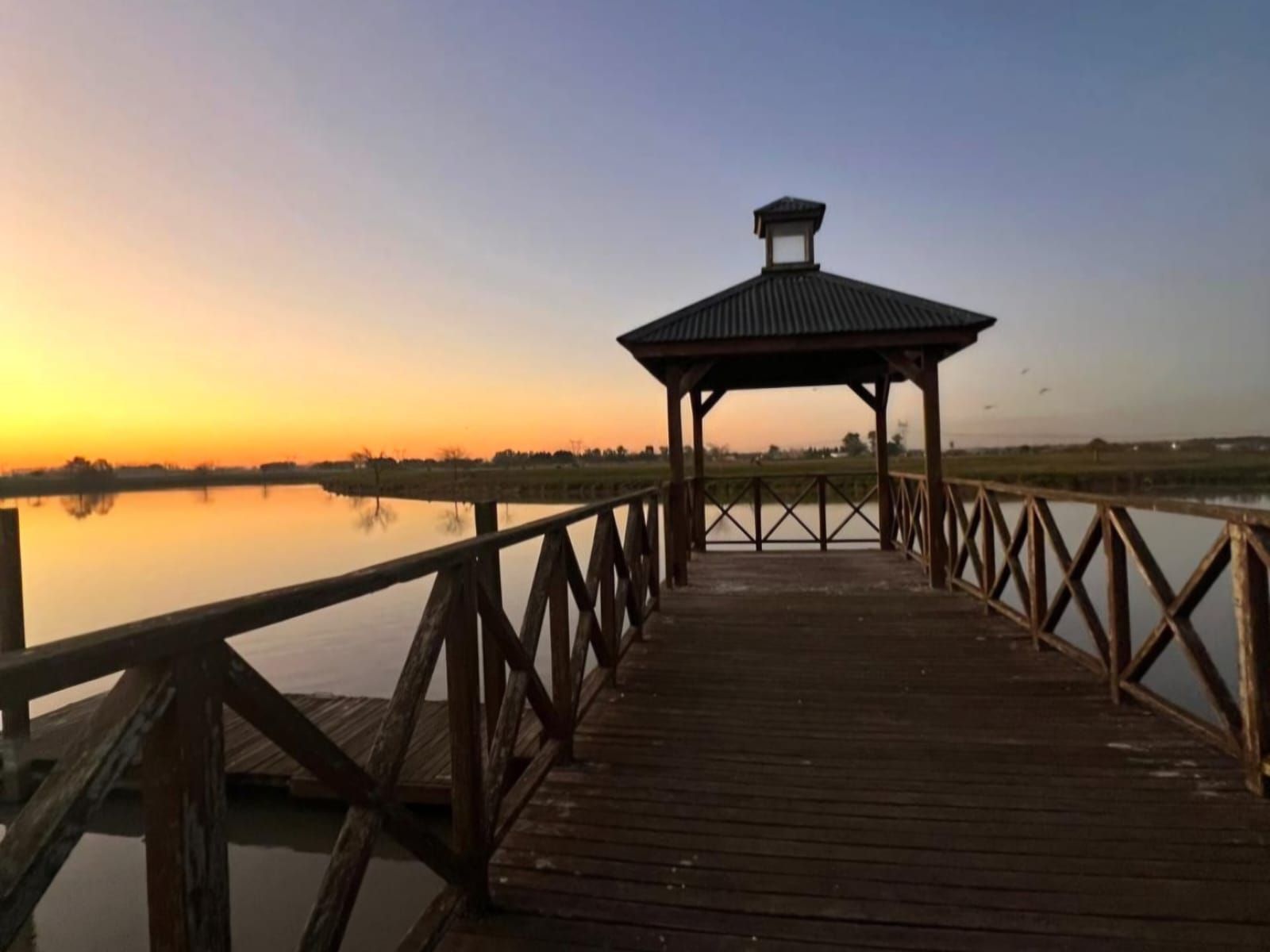Muelle de madera que conduce a un mirador al atardecer sobre aguas tranquilas.