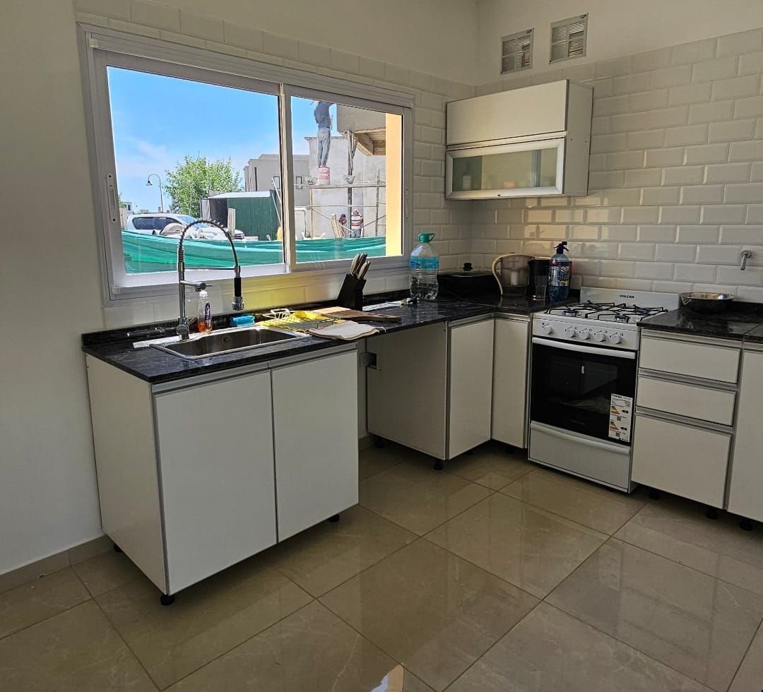 Cocina moderna con armarios blancos, encimeras negras, suelo de baldosas y una ventana con vistas al exterior.