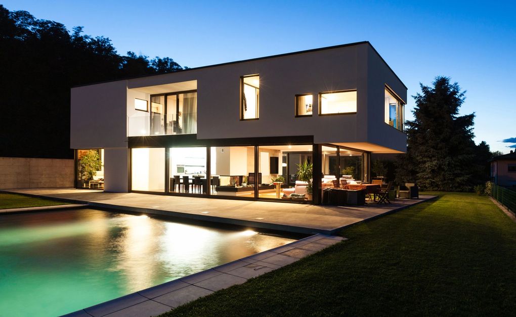 Moderna casa de dos plantas al anochecer con ventanas iluminadas y una piscina en la fachada.