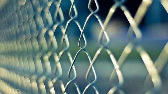 Close-up of a chain-link fence, with soft focus and a shallow depth of field, in shades of blue and silver.