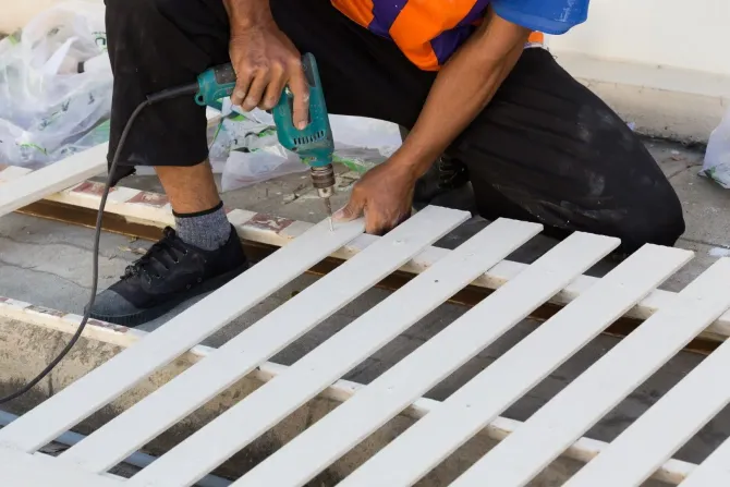 Worker drilling and repairing a white wooden fence.