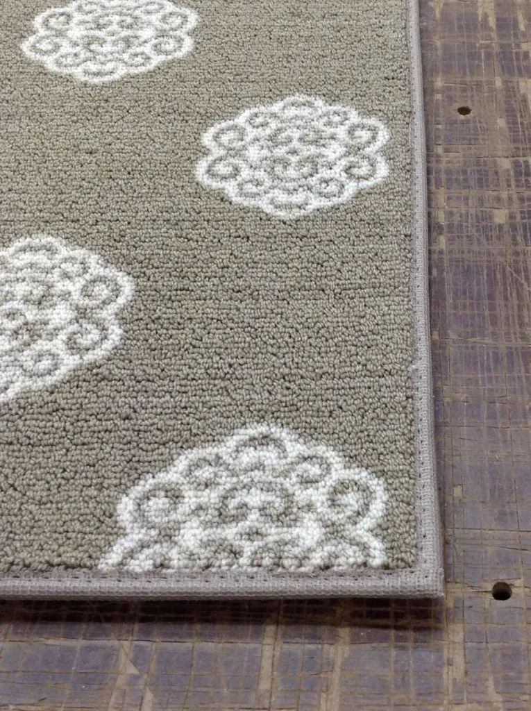 Close-up of a gray rug with white floral patterns on a dark wood floor.
