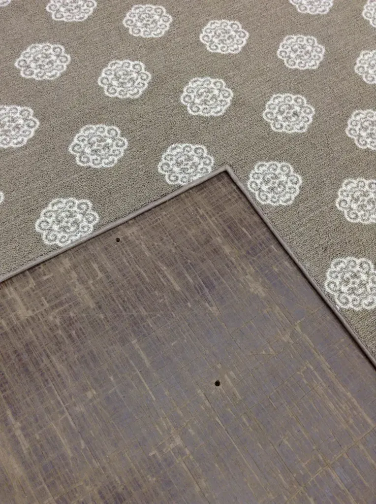 Dark wooden surface partially covering patterned gray and white carpet.
