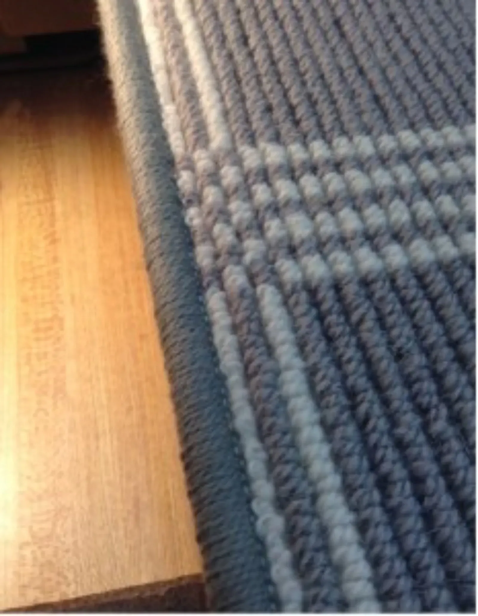 Close-up of handwoven textile in grey and white stripes with a finished edge, lying on wood.