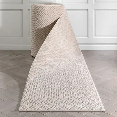 Roll of beige patterned carpet unfurling on a light wood floor, against a wall.