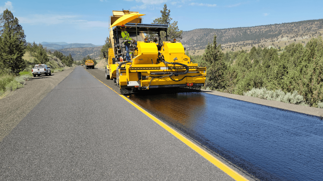 Bright yellow paving machine applying a new layer of asphalt along a long roadway surrounded by open landscape during an asphalt paving service in Arvada, CO