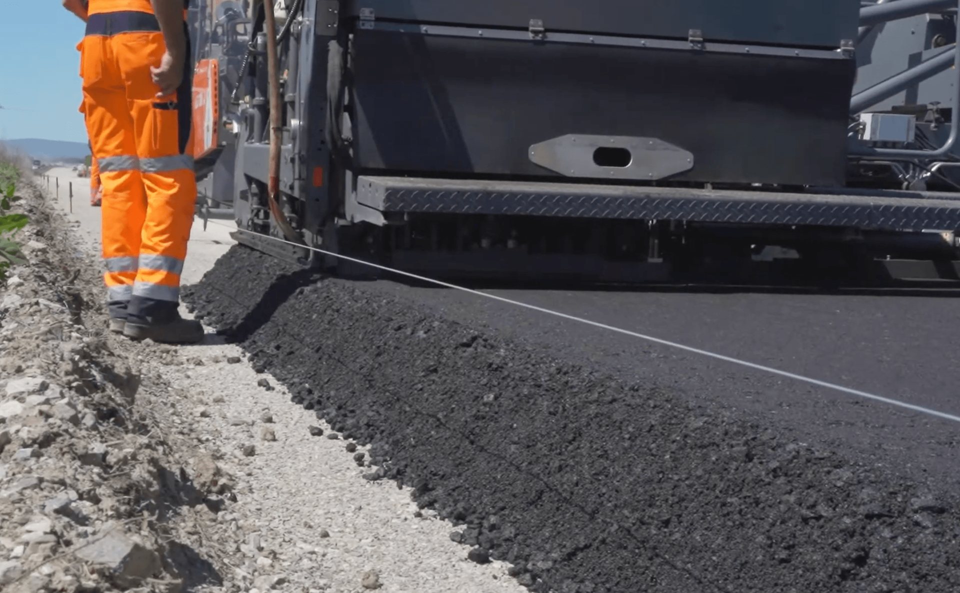 Worker guiding asphalt edge with a string line for precise alignment behind a paving machine during an asphalt paving service in Arvada, CO