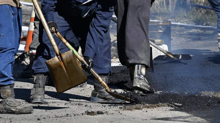 Crew using shovels to spread and level hot asphalt on a damaged road surface during an asphalt paving service in Arvada, CO