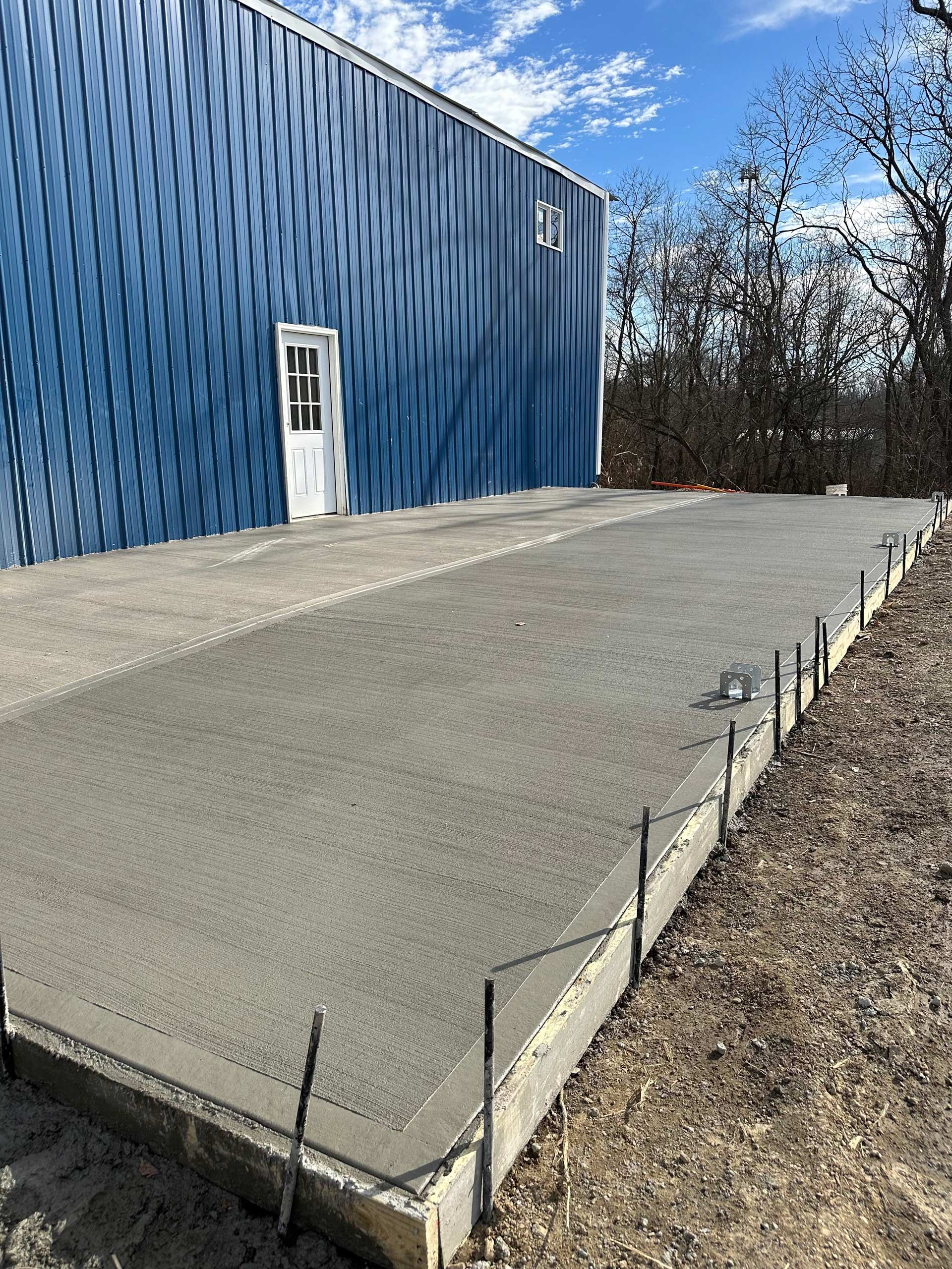 A concrete driveway is being built in front of a blue building.