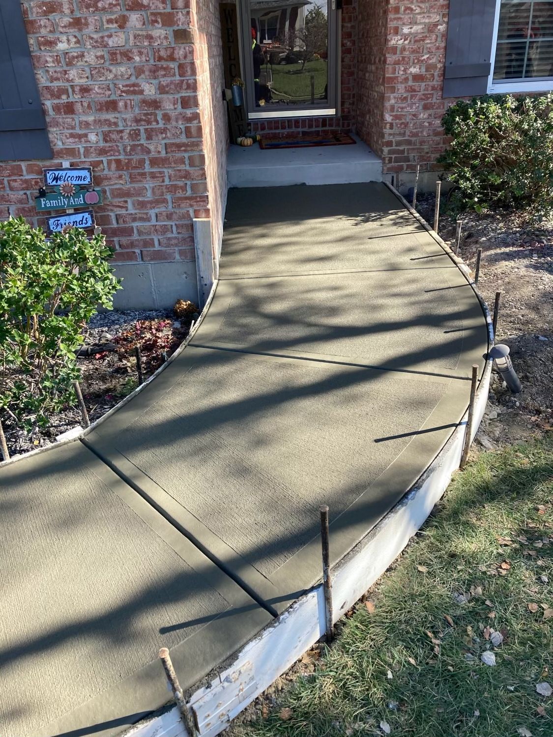 A concrete walkway is being built in front of a brick house.