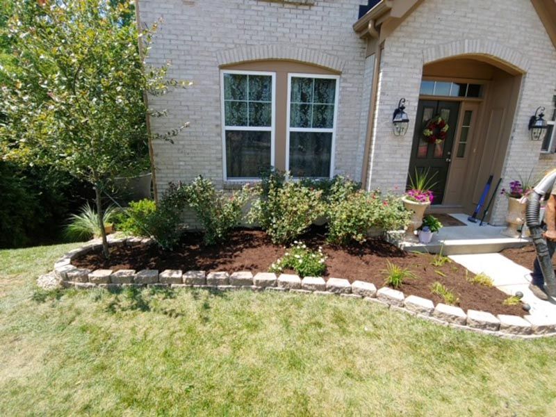 A man is standing in front of a brick house with a lush green lawn.