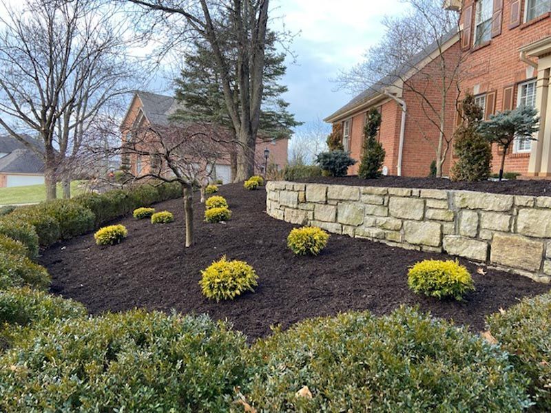 A brick wall surrounds a lush green garden in front of a brick house.