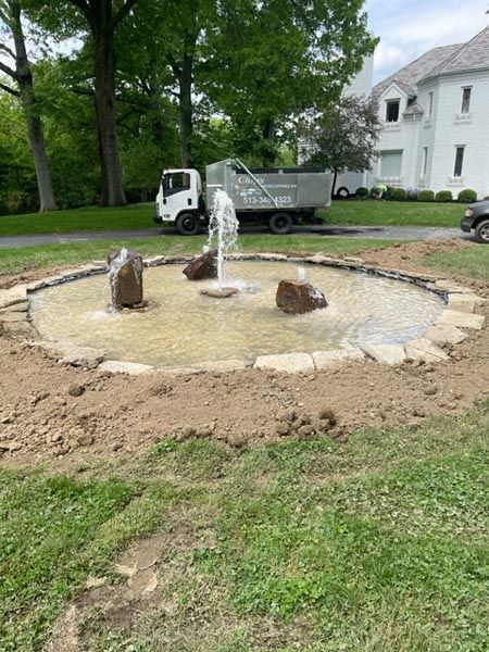 A dump truck is parked in front of a fountain in a yard.