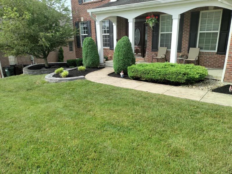 A lush green lawn in front of a brick house with a porch.