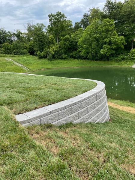 A concrete wall is sitting on top of a lush green field next to a lake.
