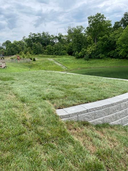 A lush green field with a brick wall and a lake in the background.