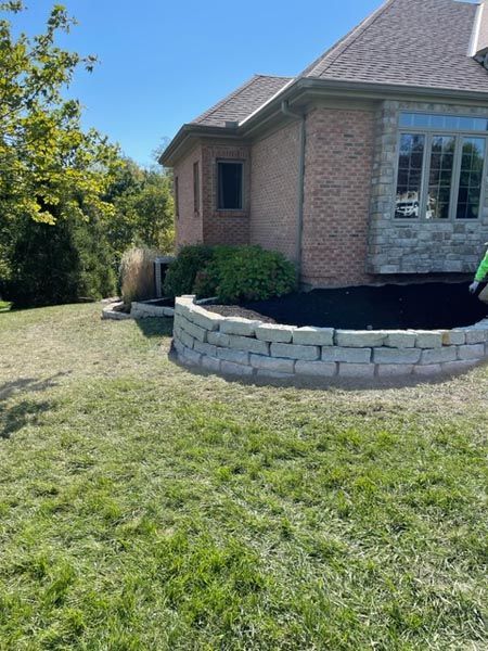 A man is standing in front of a house with a brick wall in front of it.