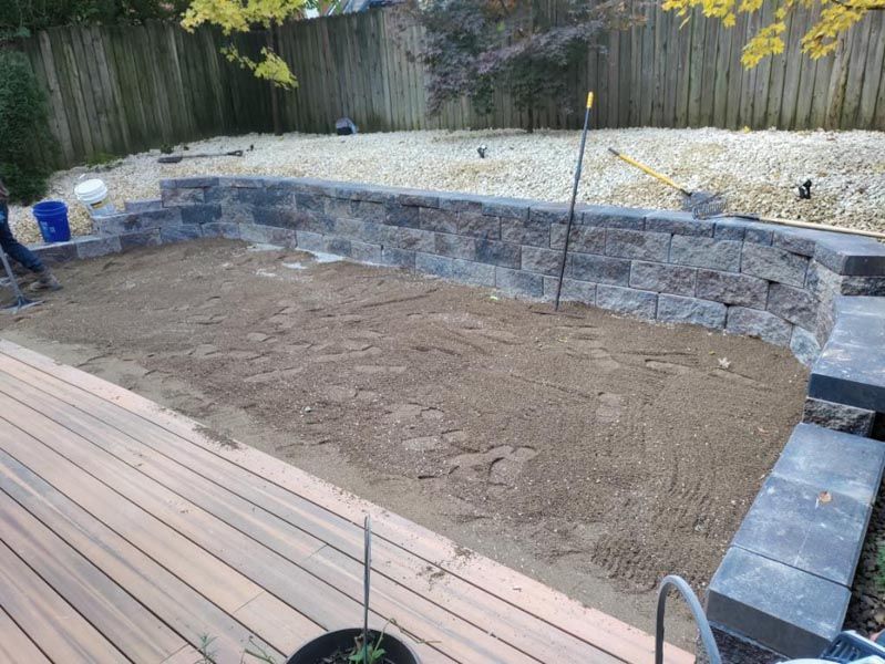 A brick wall is being built in a backyard next to a wooden deck.