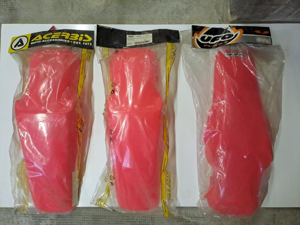 Tre paraurti rossi in plastica sono appoggiati su una superficie bianca.