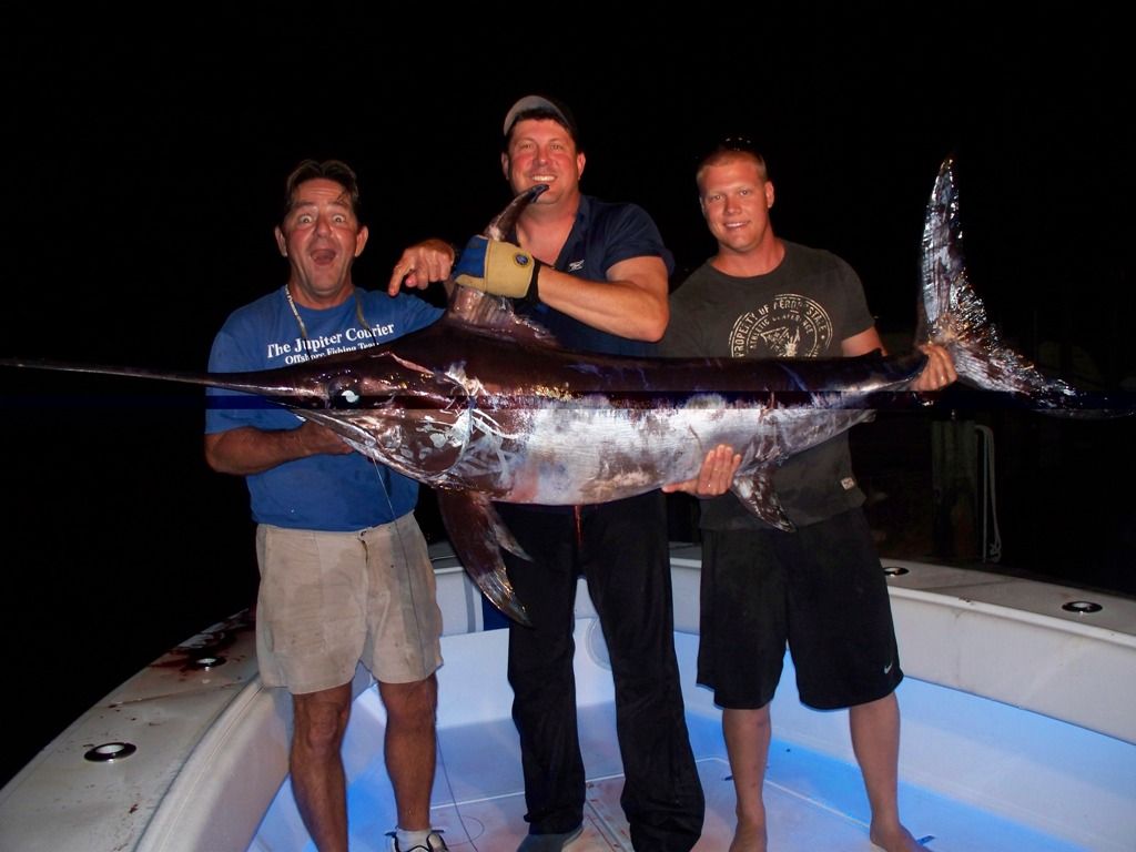 Three men standing on a boat holding a large fish