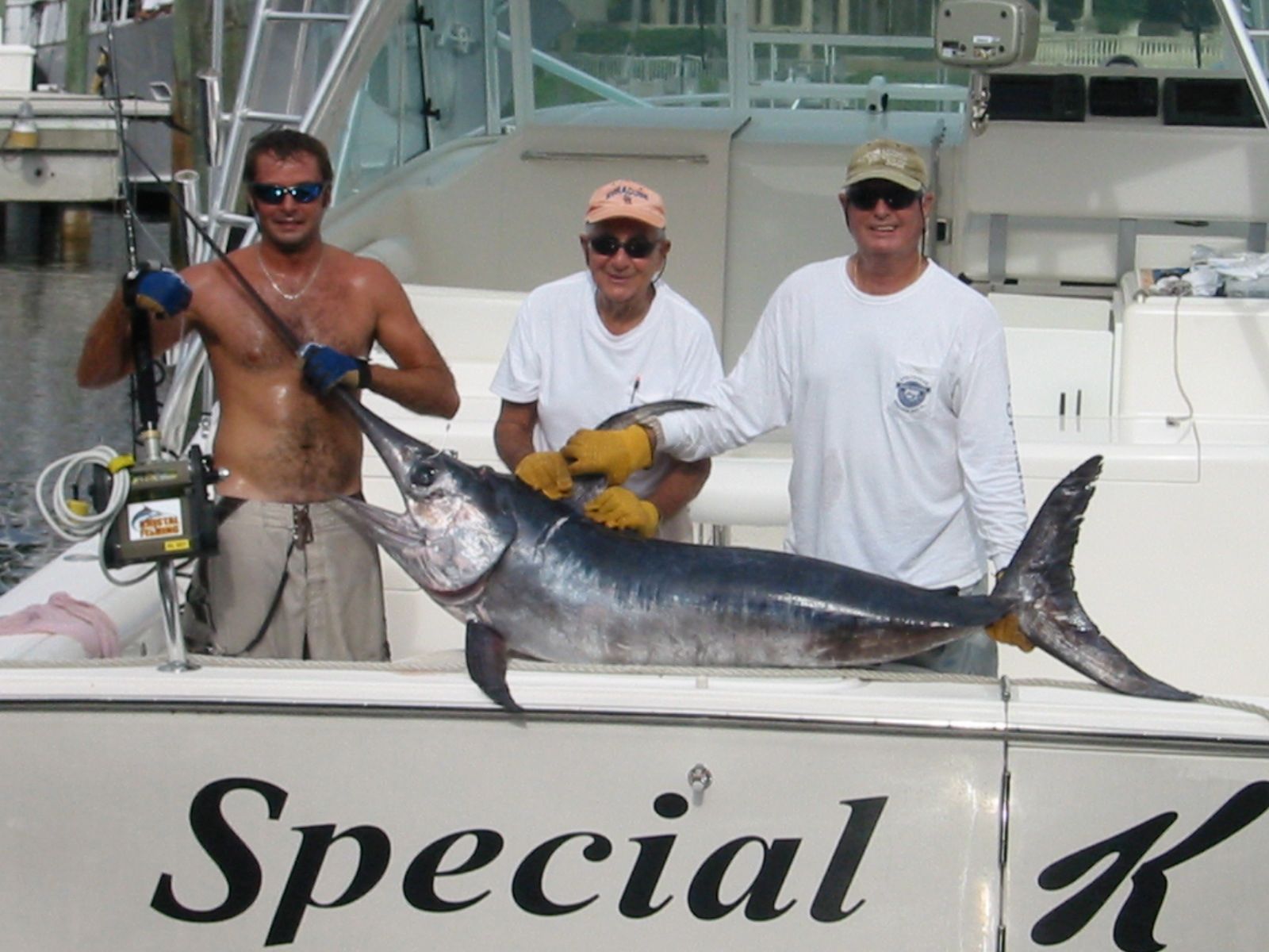 Three men standing next to a large fish on a boat that says special k