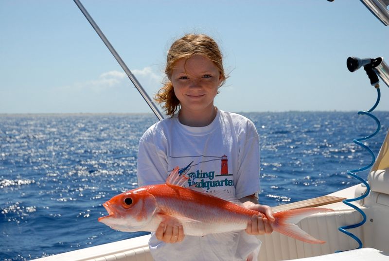A young girl is holding a fish on a boat with a shirt that says central headquarters