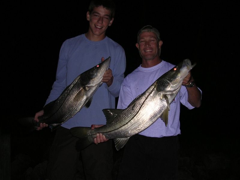 Two men are holding two large fish in their hands