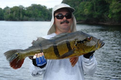 a man holding a large fish in front of a body of water