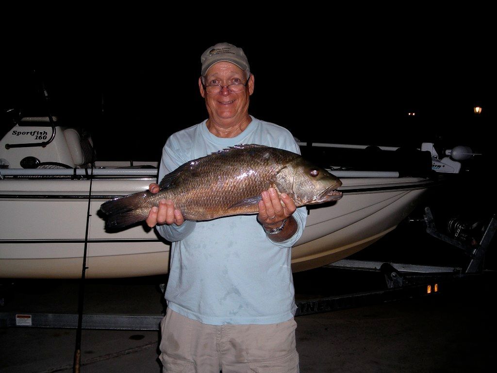 A man is holding a large fish in front of a boat with the letters t on it