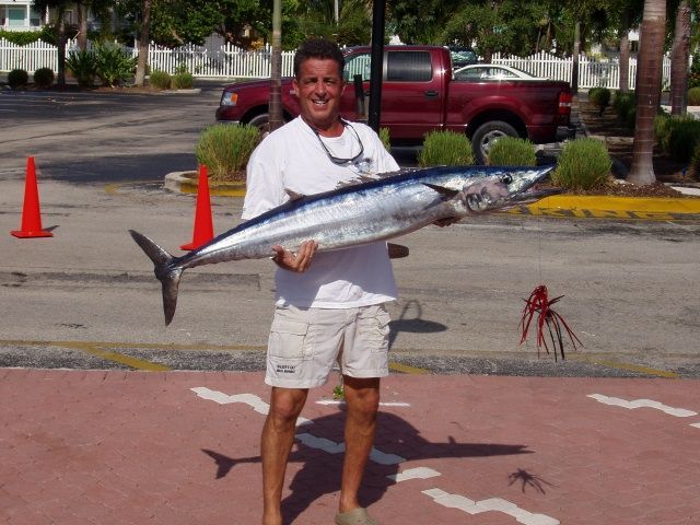 A man is holding a large fish in a parking lot