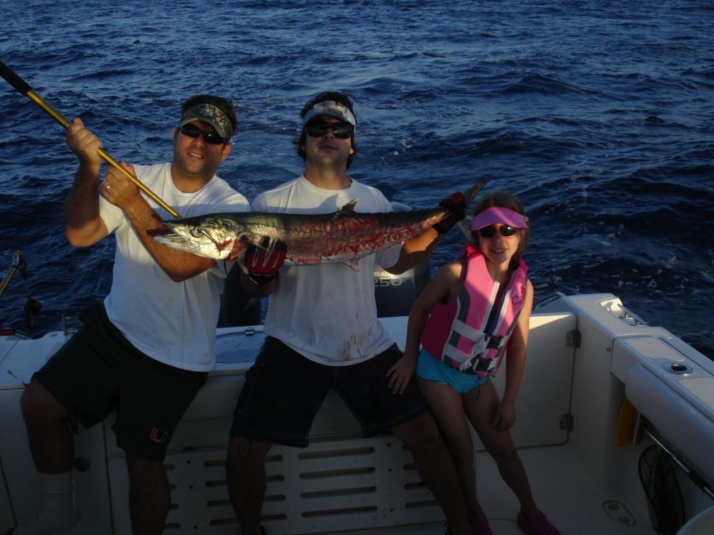 Two men and a girl holding a large fish on a boat