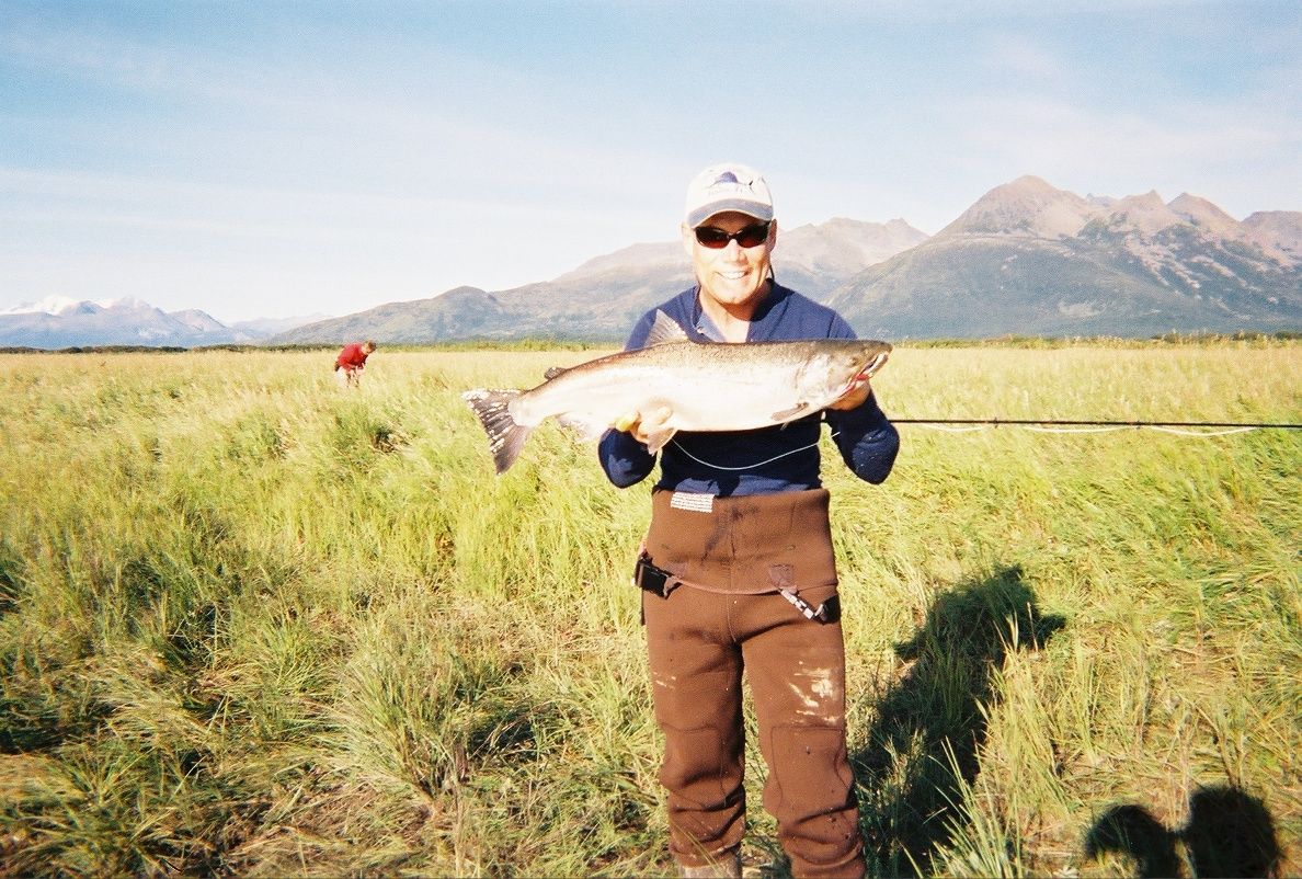 A man holding a fish in a field with mountains in the background