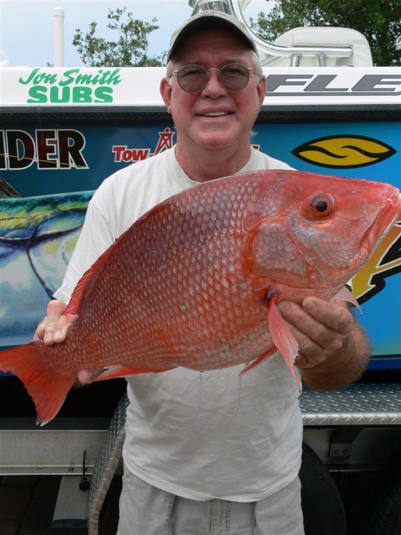 A man is holding a large red fish in front of a sign that says jon smith subs