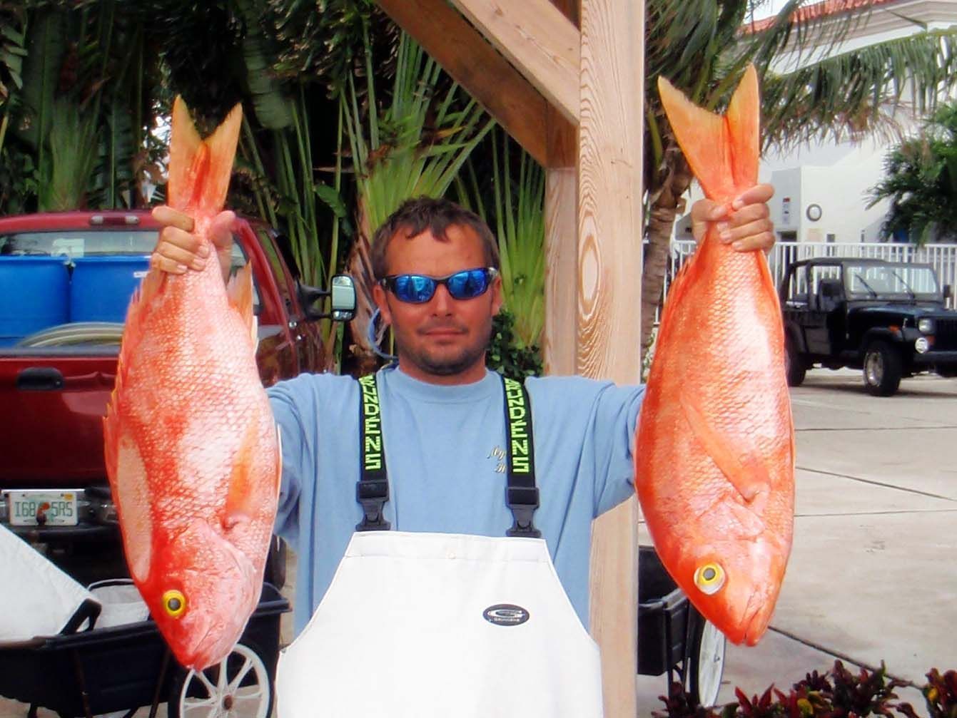A man holding two large red fish wearing a shirt that says mizuno