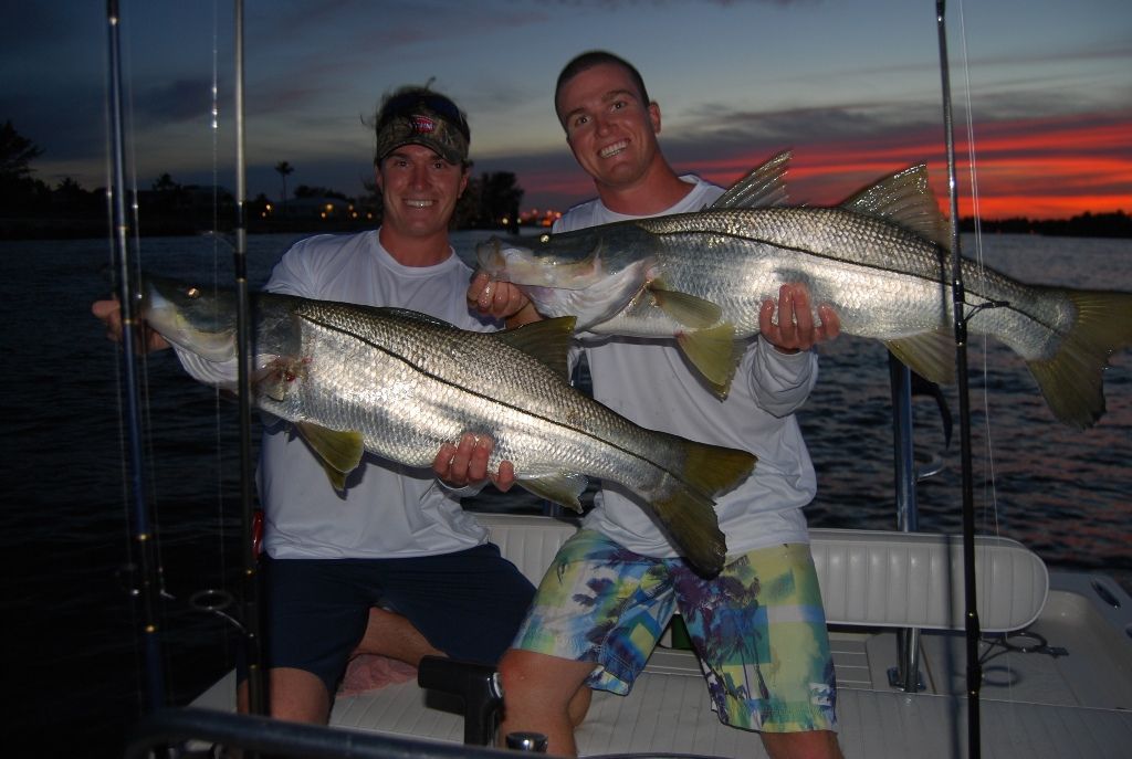 Two men sitting on a boat holding large fish