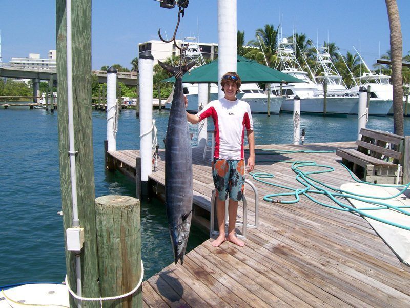 A boy stands on a dock holding a large fish